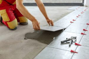 CERAMICAS Ceramic Tiles. Tiler placing ceramic wall tile in position over adhesive with lash tile leveling system - Image