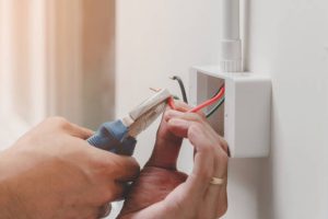 The technician is using a pliers wrench to install the power plug on the wall. The technician is using a pliers wrench to install the power plug on the wall.