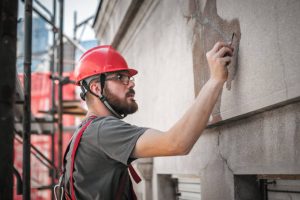 HORMIGON Man worker standing on scaffolding, perform work on the restoration of the facade of the old building. Repairing and renovate